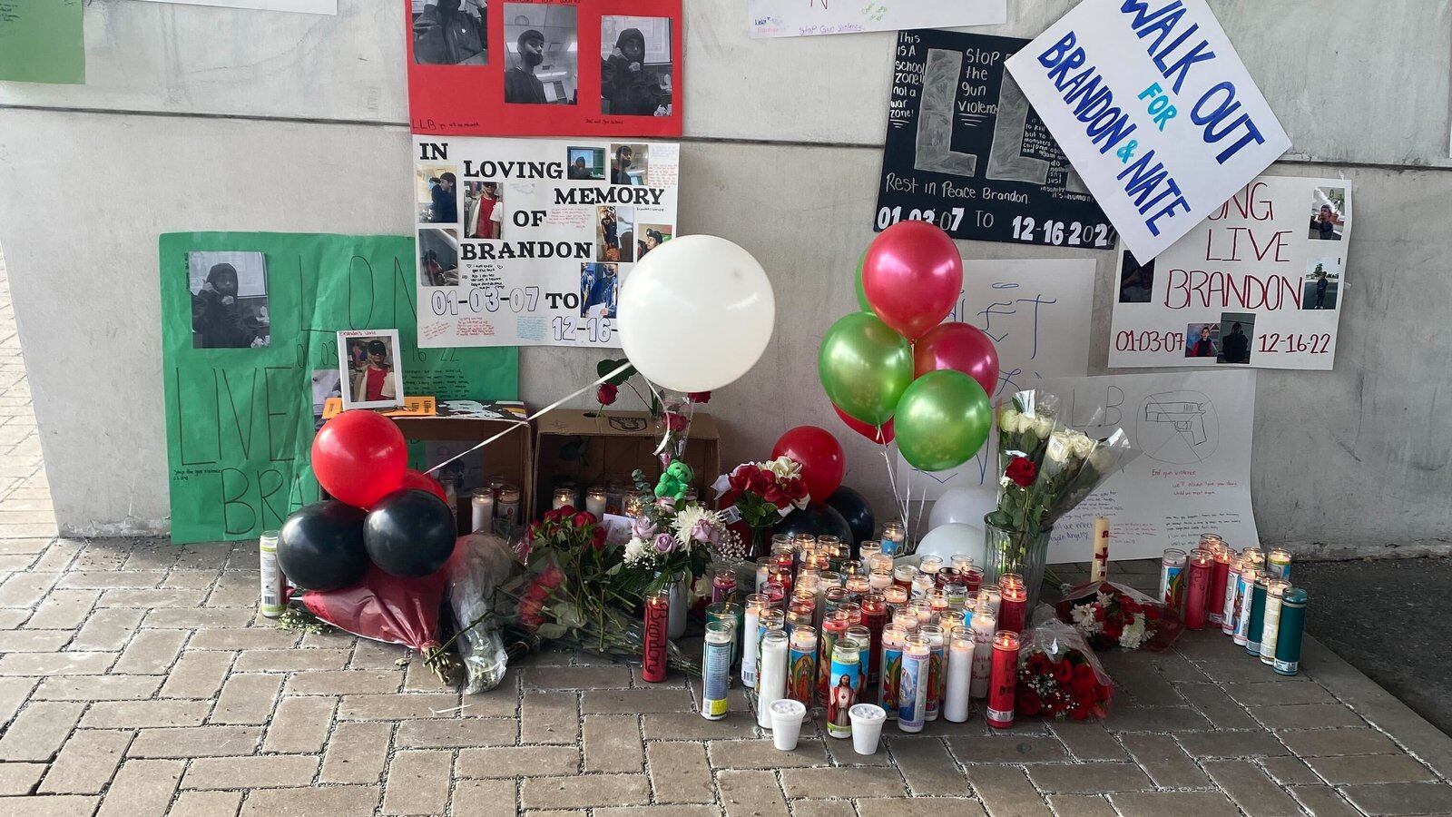 Signs mentioning Brandon Perez and Nathan Billegas hang on the wall. On the ground, there are balloons, candles, and flowers for a memorial to the two students at Benito Juarez High School in Chicago.