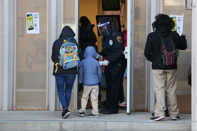 School guard take students’ temperature at the entrance to Camden Street Elementary School.