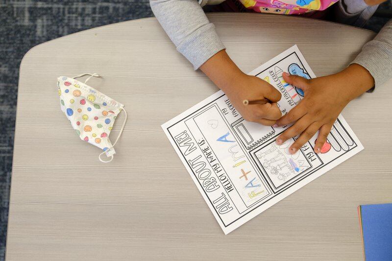 A mask sits next to a student as they complete a worksheet. The photo is zoomed in on the worksheet and the student’s hands.