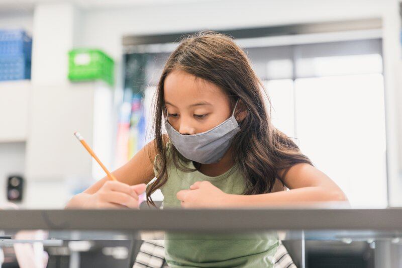 A girl in a mask works at a desk with a pencil in one hand.