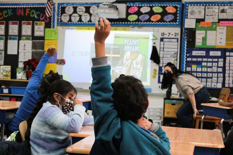 Students raise their hands in the classroom, with the text “Plains Indians” projected on the white board at the front of the class.
