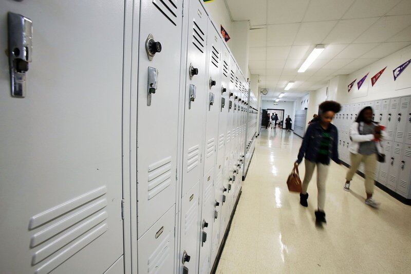 Students walk past white lockers in a school hallway