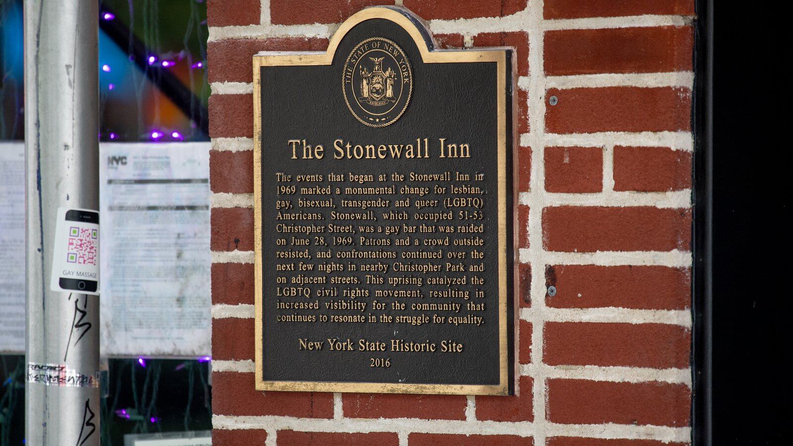 A black and gold sign on a brick wall denotes the Stonewall Inn in New York City as a New York State Historic Site.