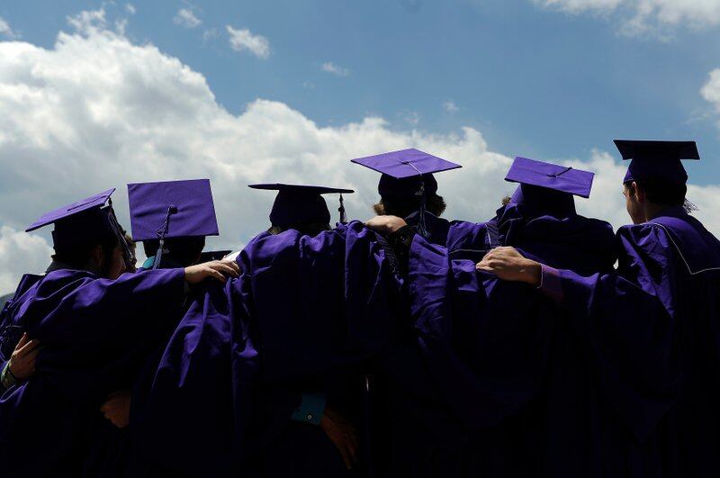 The backs of six students in purple caps and gowns in a line with their arms around each others’ shoulders.
