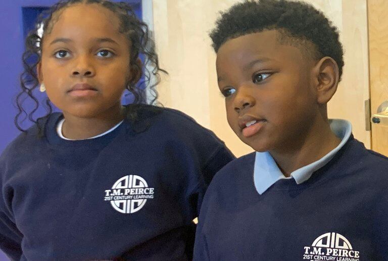 Two children wearing dark blue school uniforms stand next to each other.