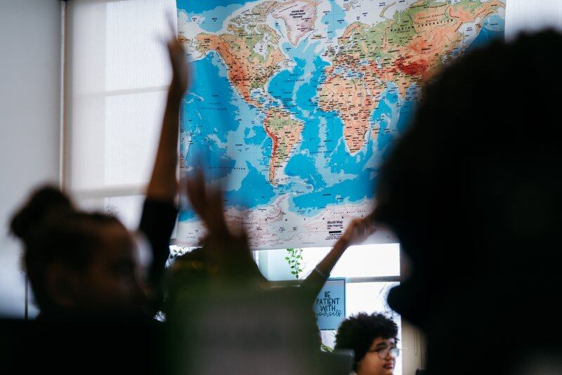 Silhouettes of students with their hands raised in front of a map.