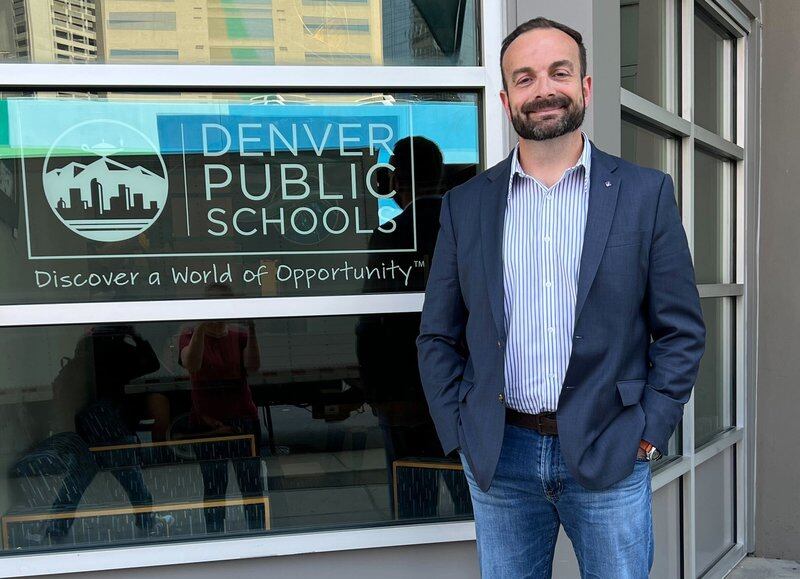 a man in a jacket and jeans stands outside Denver Public Schools headquarters