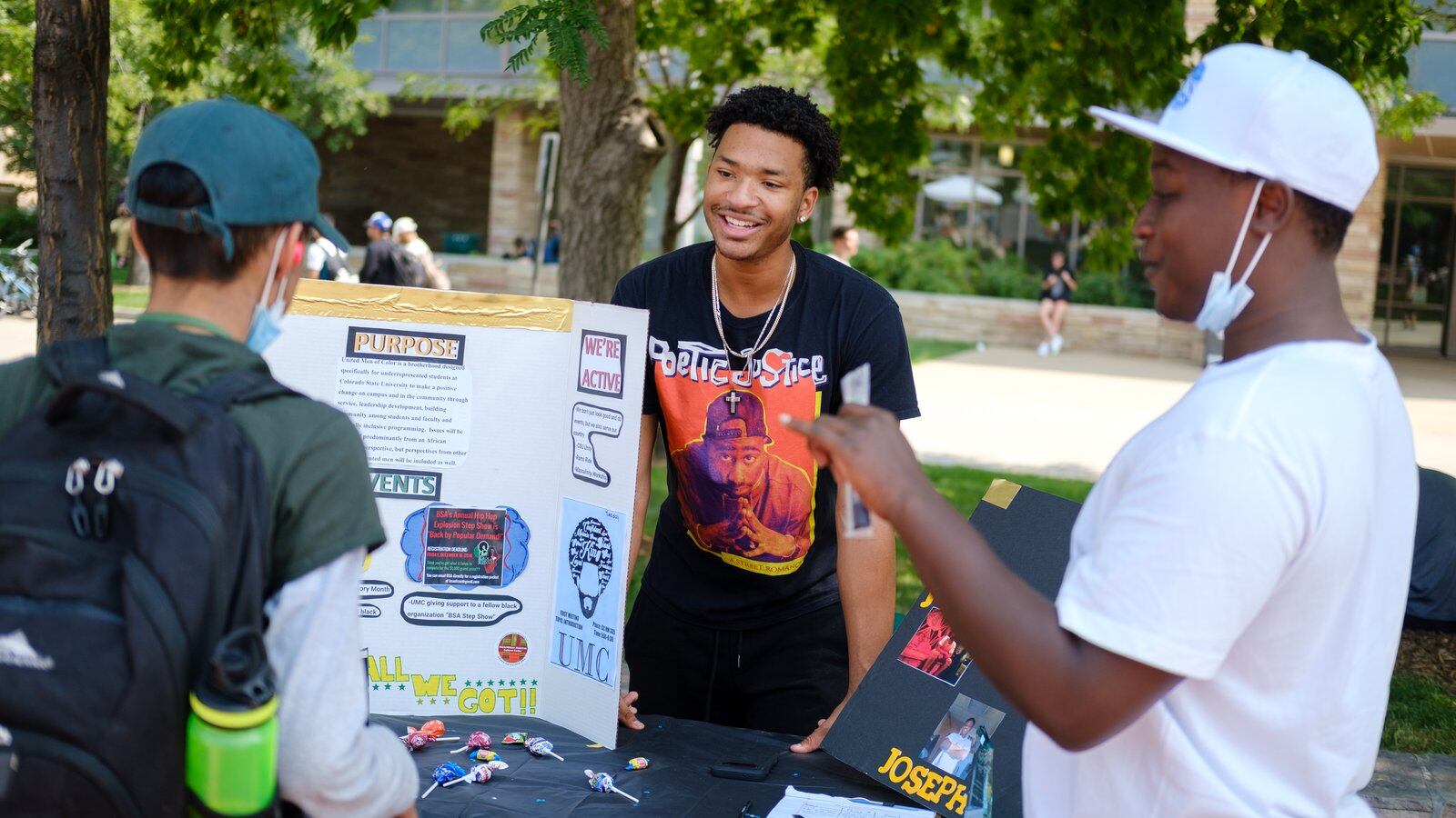 Two young men talk to a fellow student student about their on-campus group, United Men of Color, during a student involvement fair.