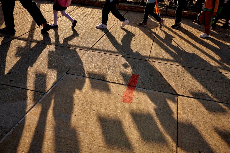A line of children’s shadows and a fence on the ground outside of a school.