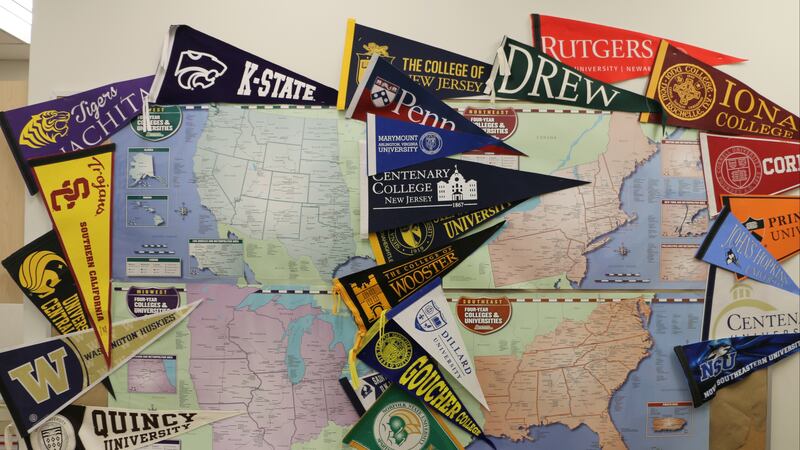 A wall is decorated with college pennants surrounding maps of different parts of the United States.