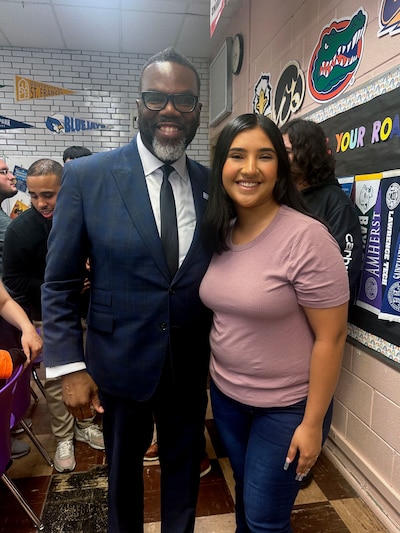 An adult man wearing a dark suit poses for a portrait with a high school senior wearing a pink shirt.