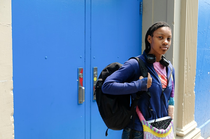 A girl in a blue sweatshirt stands in front of two blue doors.