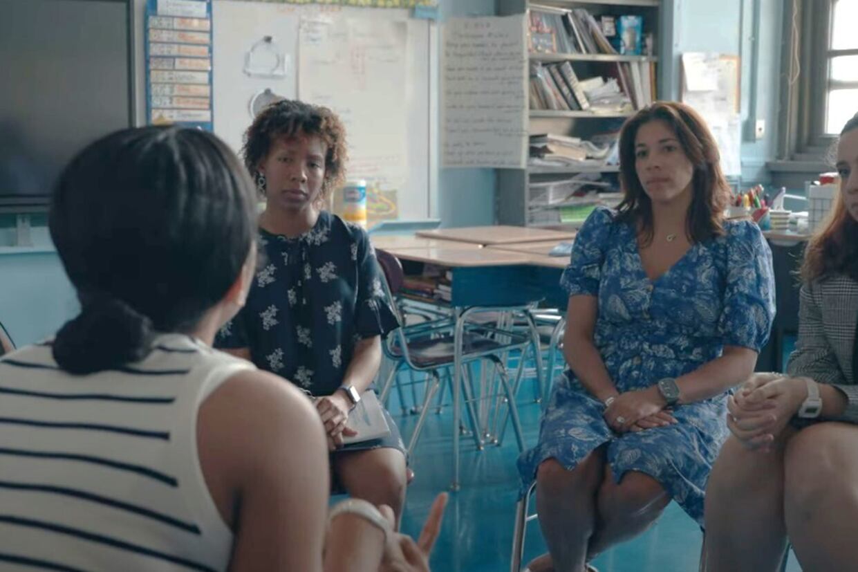 A group of people sit on chairs in a circle in a schoolroom.