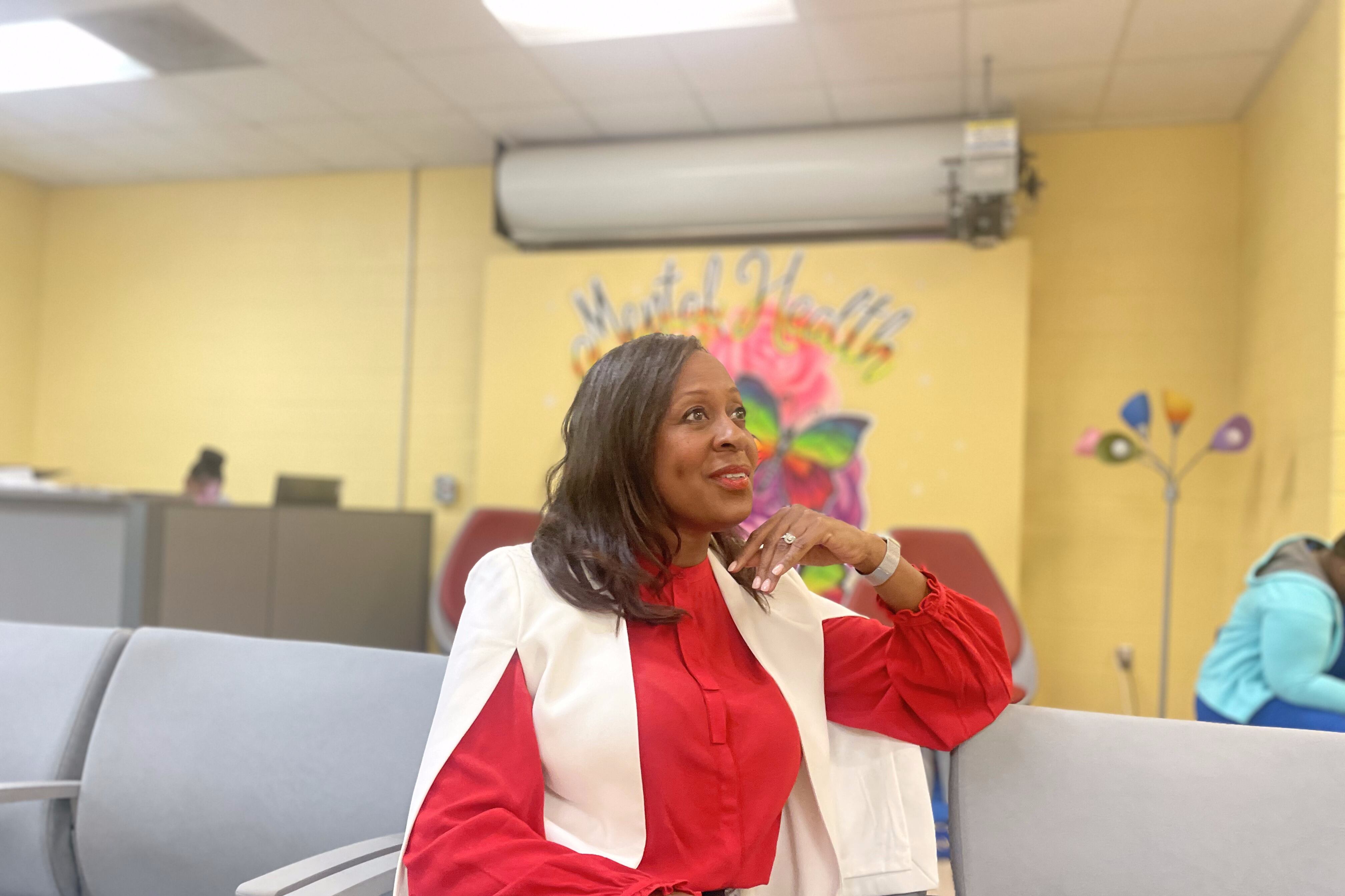 A woman sits in a blue chair; in the background, a wall mural says “mental health matters”