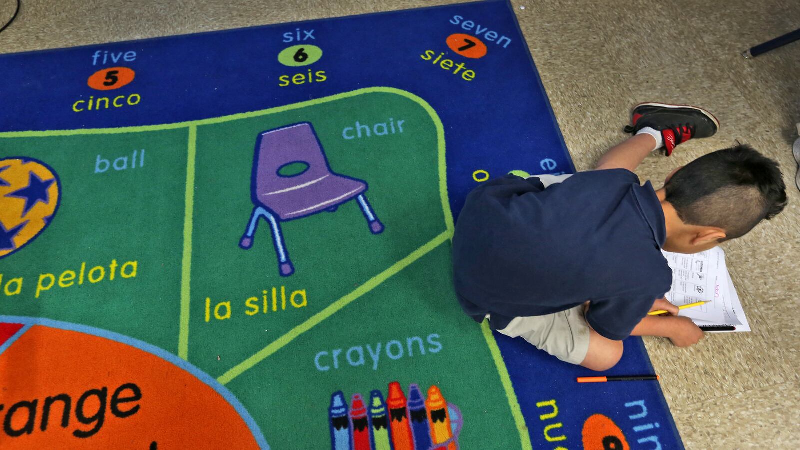 A first grader does his work while sitting on a bilingual rug at Enlace Academy, Tuesday, April 14, 2014.  The charter school, with 55 percent English-language learners, uses a blended language learning approach.