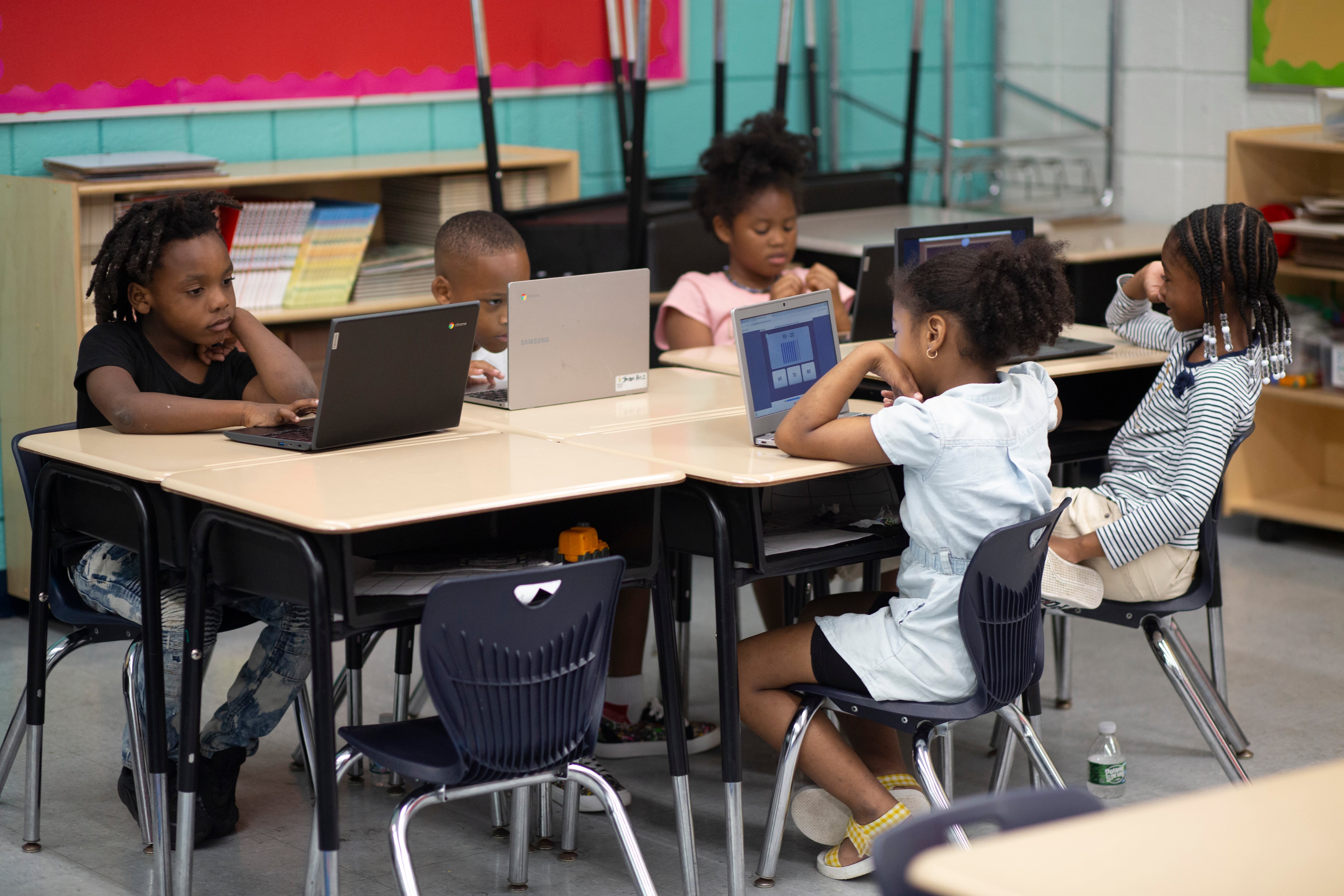 Five children sit at a table with laptops in front of each of them