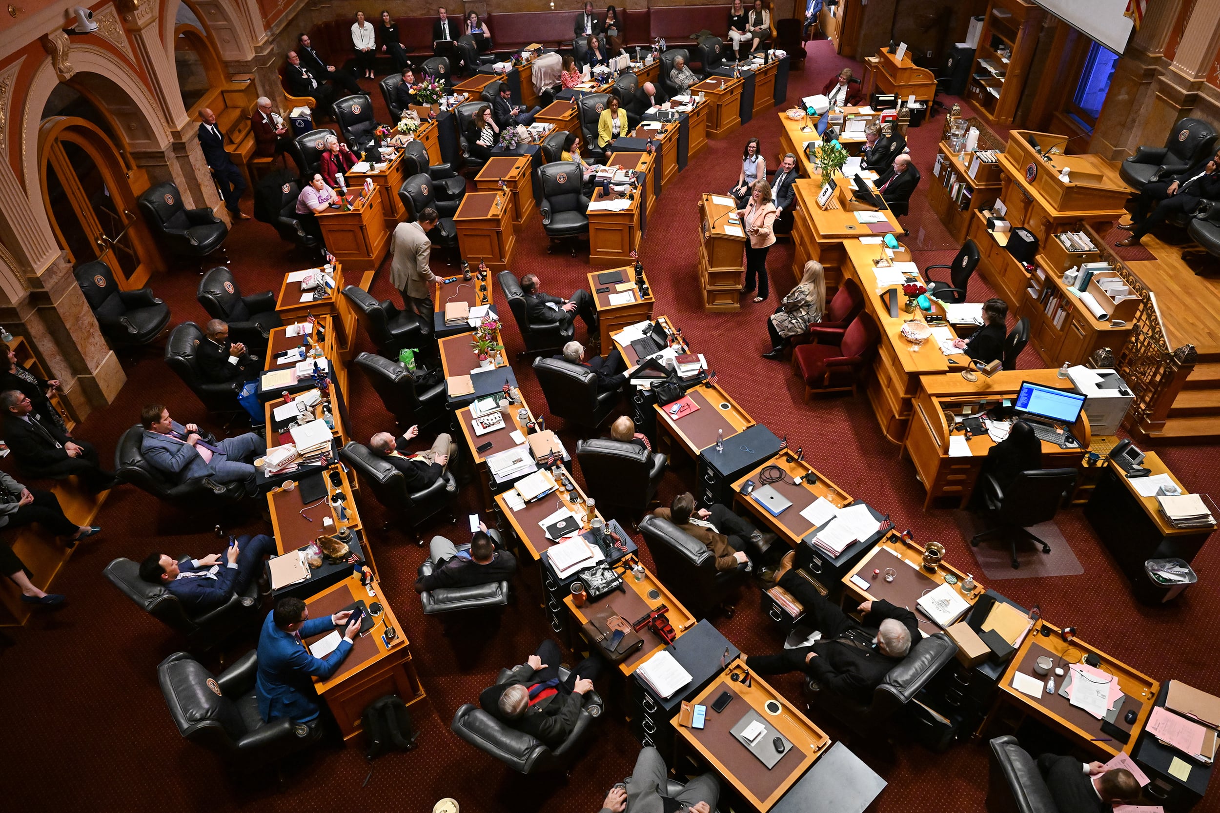 The Colorado State Capitol legislative room full of people sitting at wooden desks.
