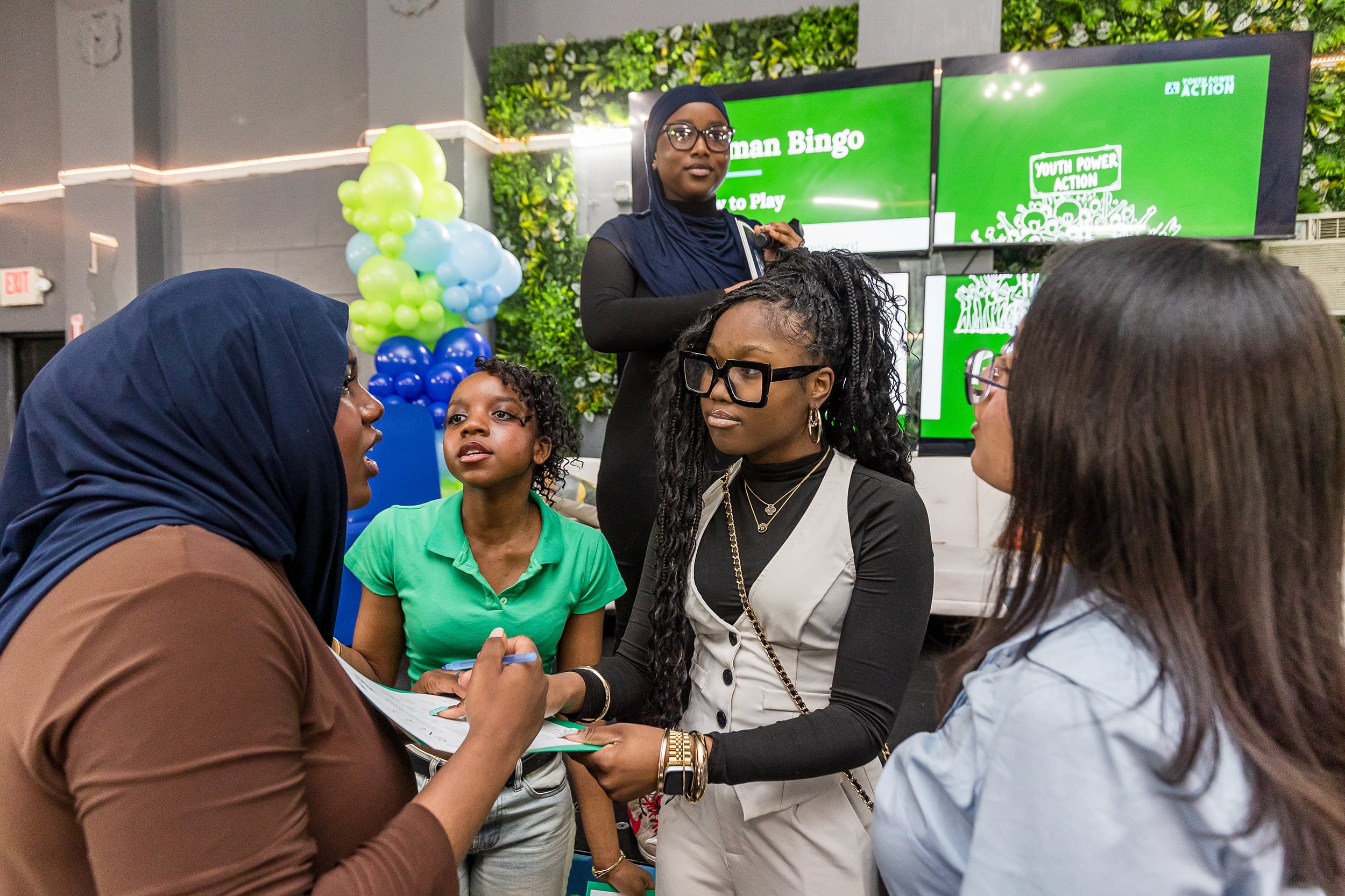 A photograph of five Black and brown female students in business clothes standing together in an event room.