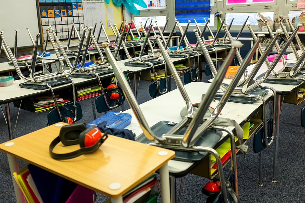 An empty classroom with chairs upside down on desks.