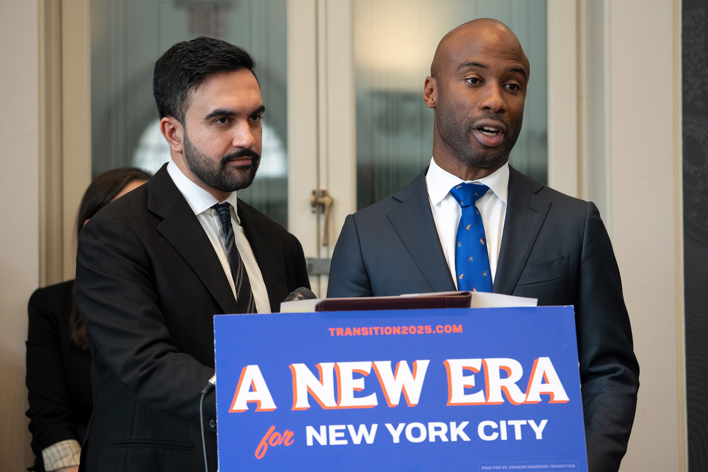 Two men in suits are standing behind a podium facing forward.