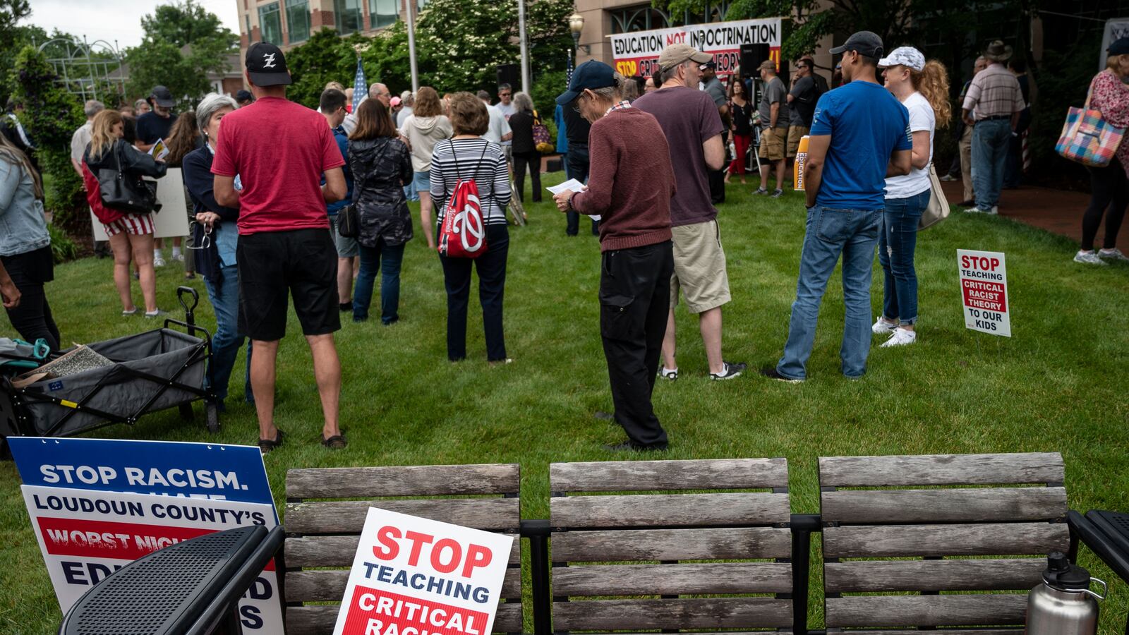 A protest against “Critical Race Theory” in front of a governmental building, with signs sitting on a row of benches in the foreground.