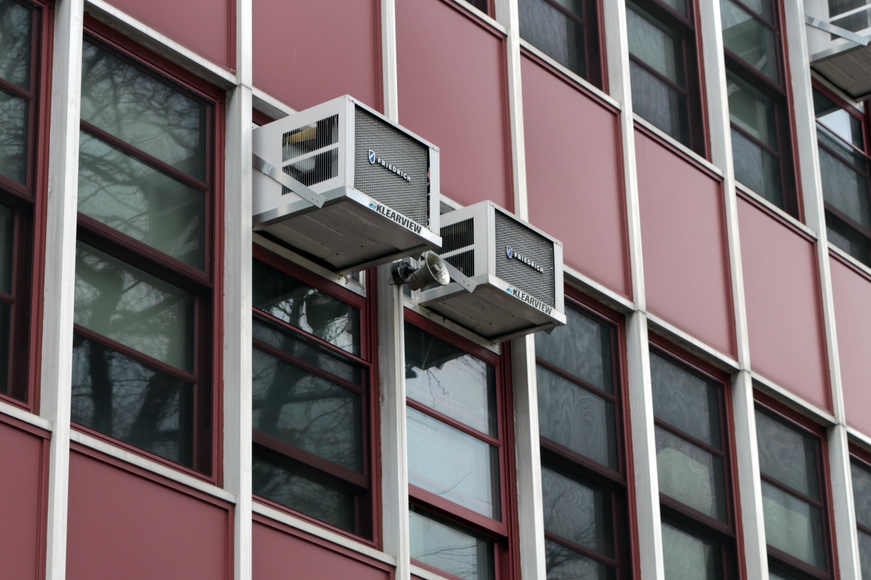 Three air conditioning boxes hang outside glass windows of a building