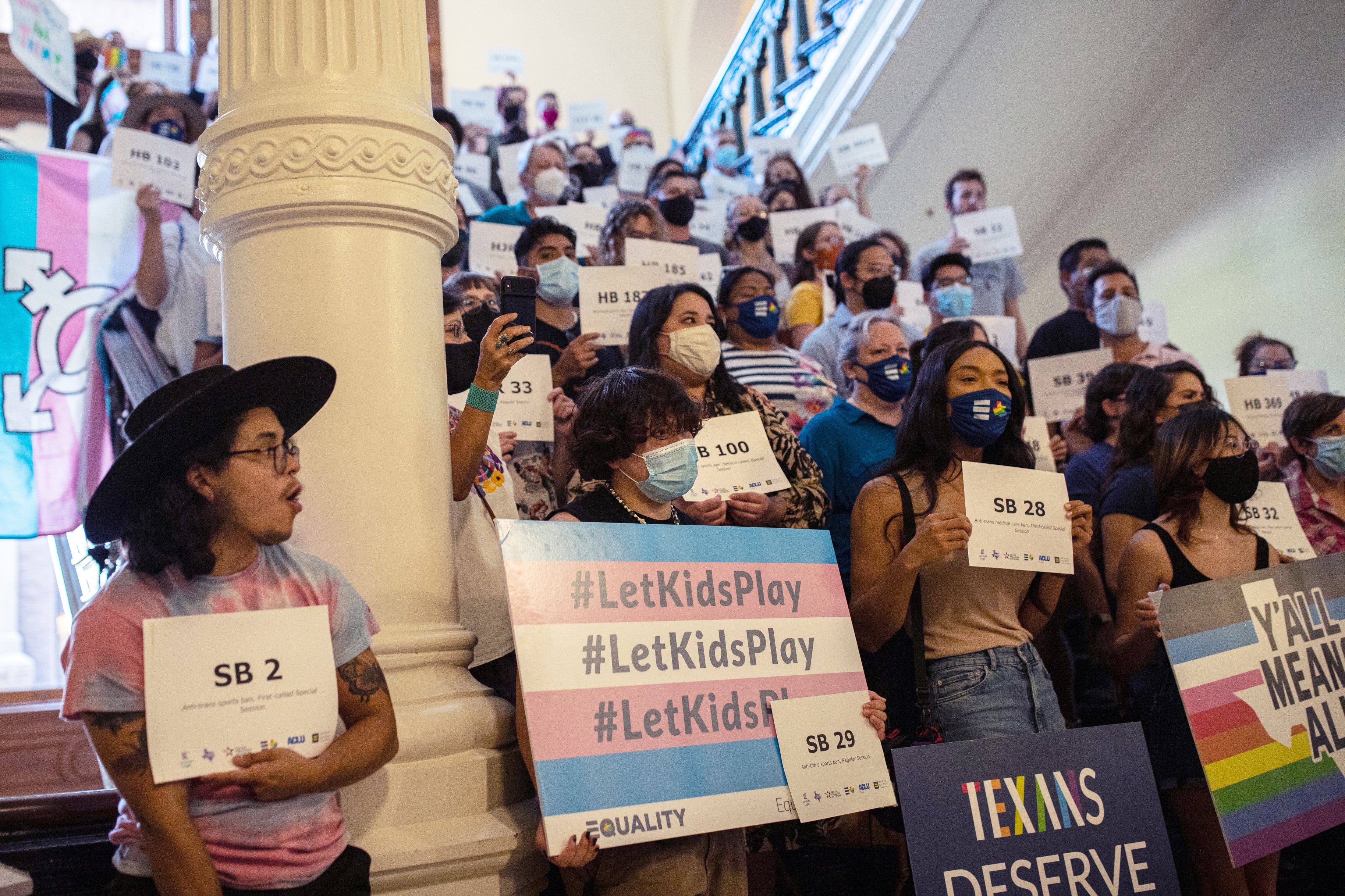A group of people organized inside a capitol building holding signs and wearing masks.