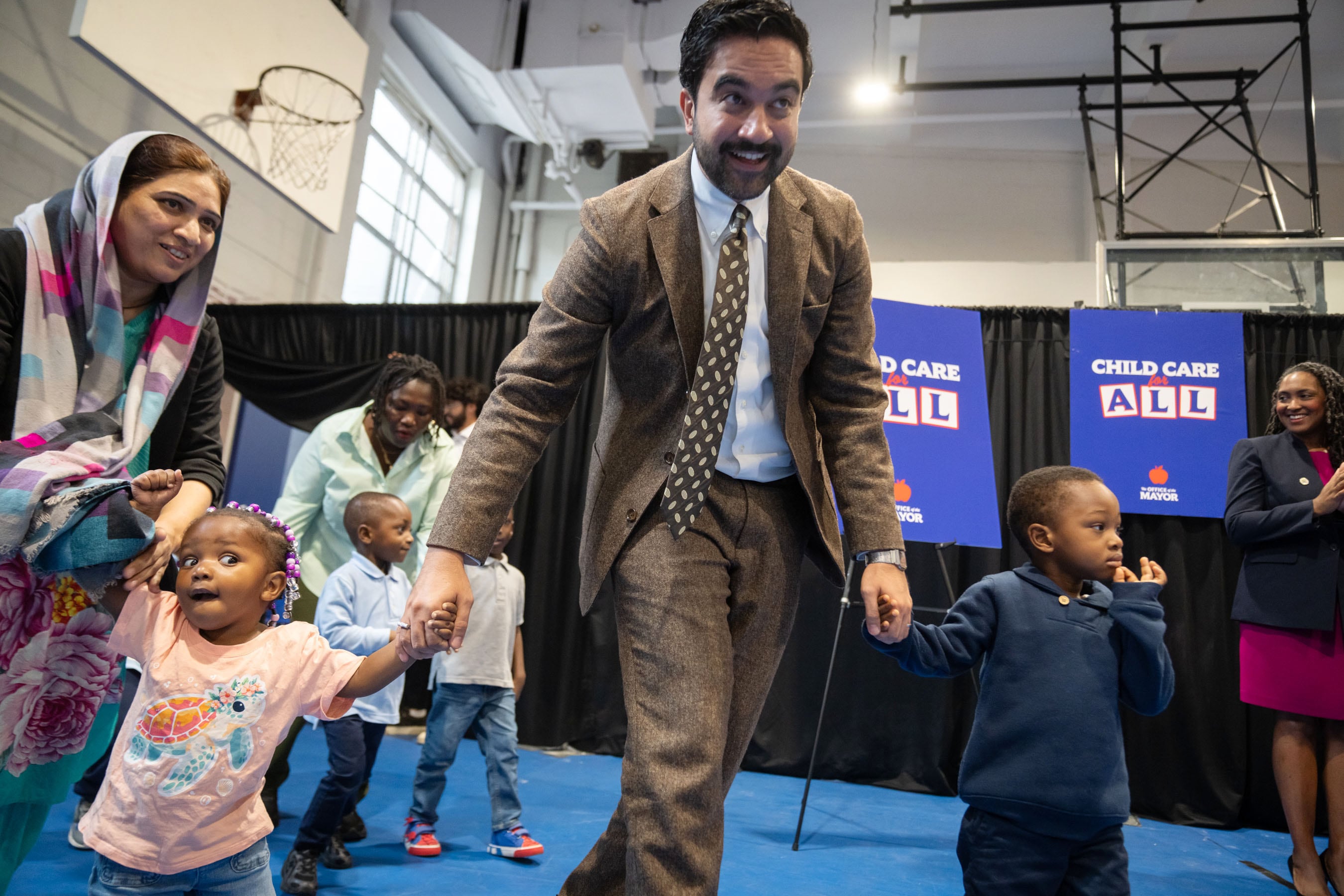 A man in a suit holds the hands of two young children during a press conference.
