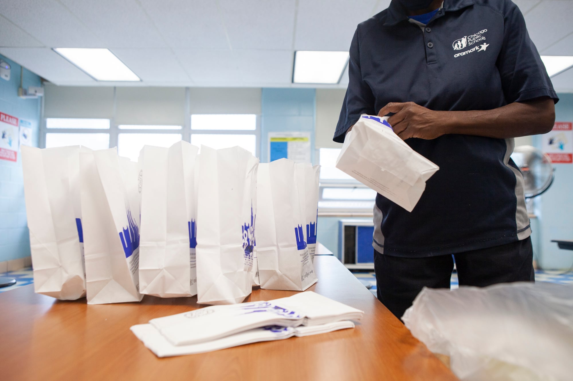 A food service worker assembles lunch bags.