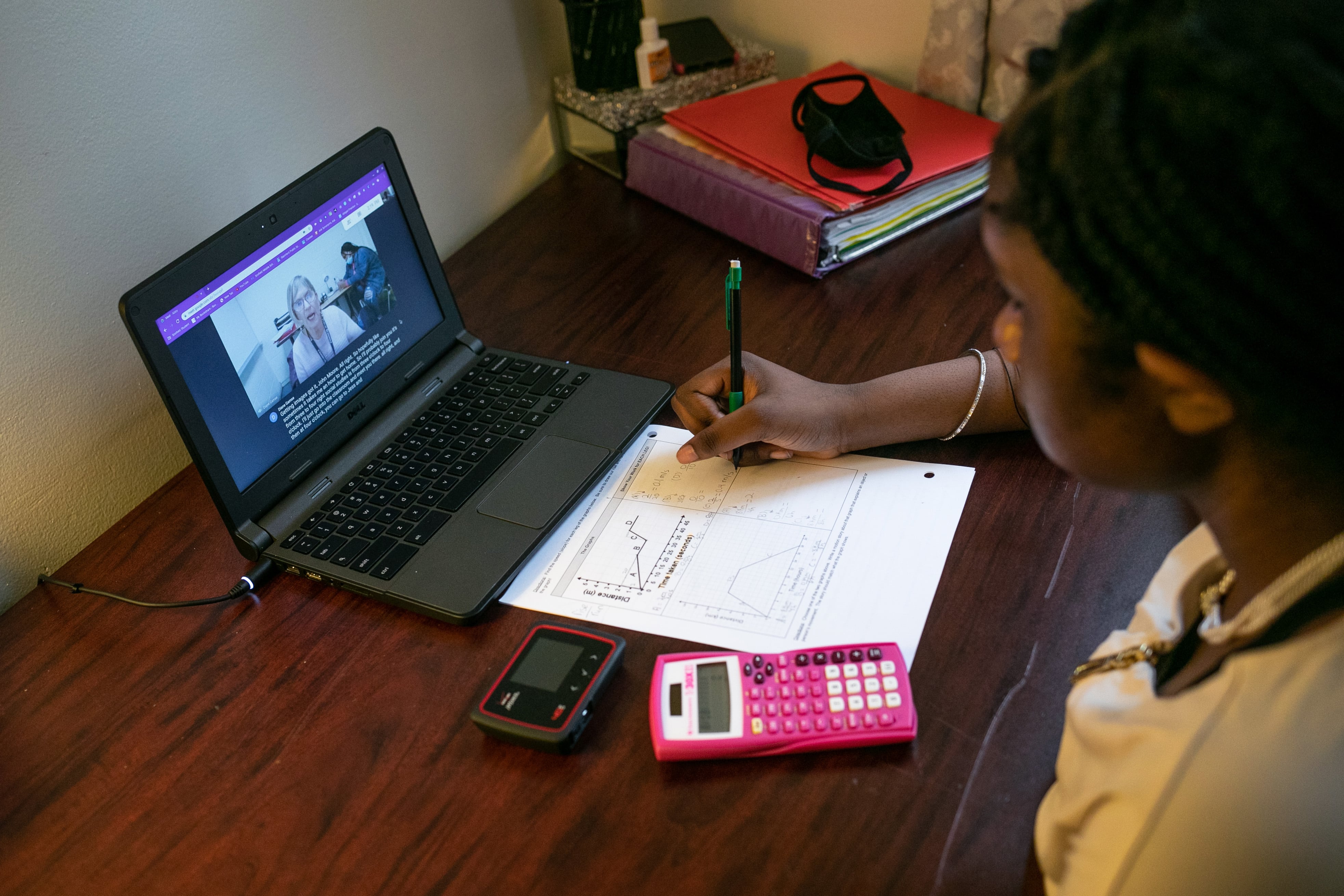 A Deaf student works with a teacher over her laptop at home. She is writing notes next to a pink calculator.