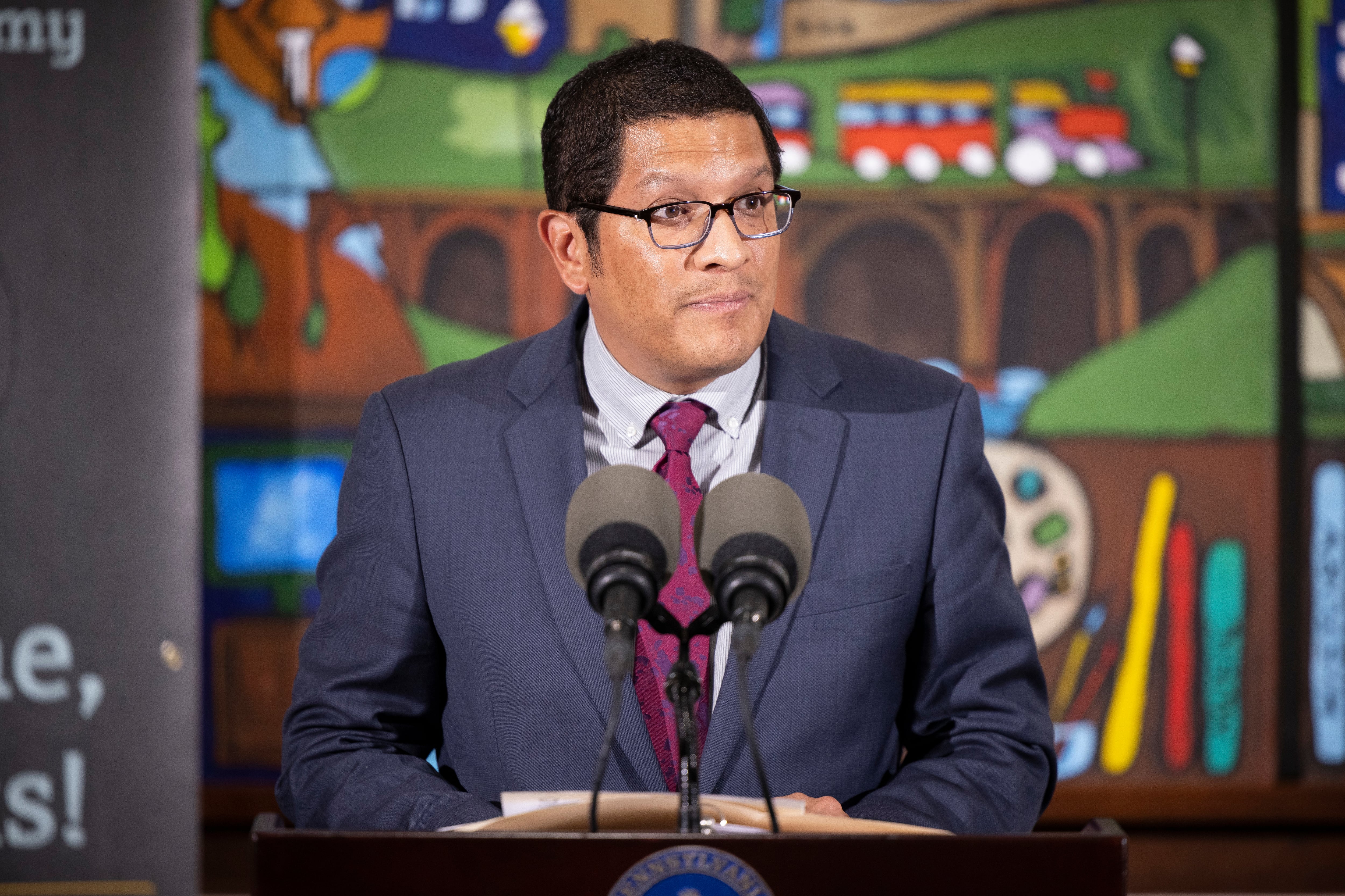 Standing in front of a colorful mural, Pennsylvania secretary of education Noe Ortega answers questions during a press conference.