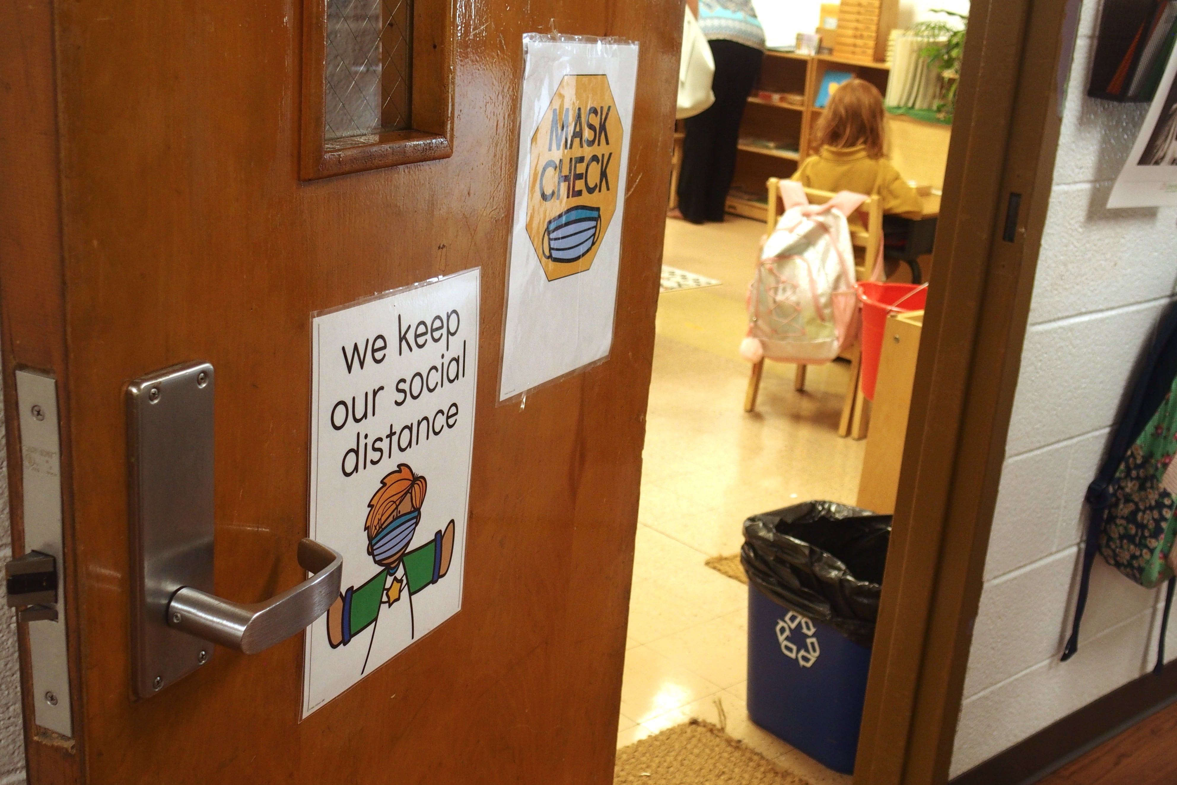 A classroom door with two signs: one says “mask check” and the other says “we keep our social distance”