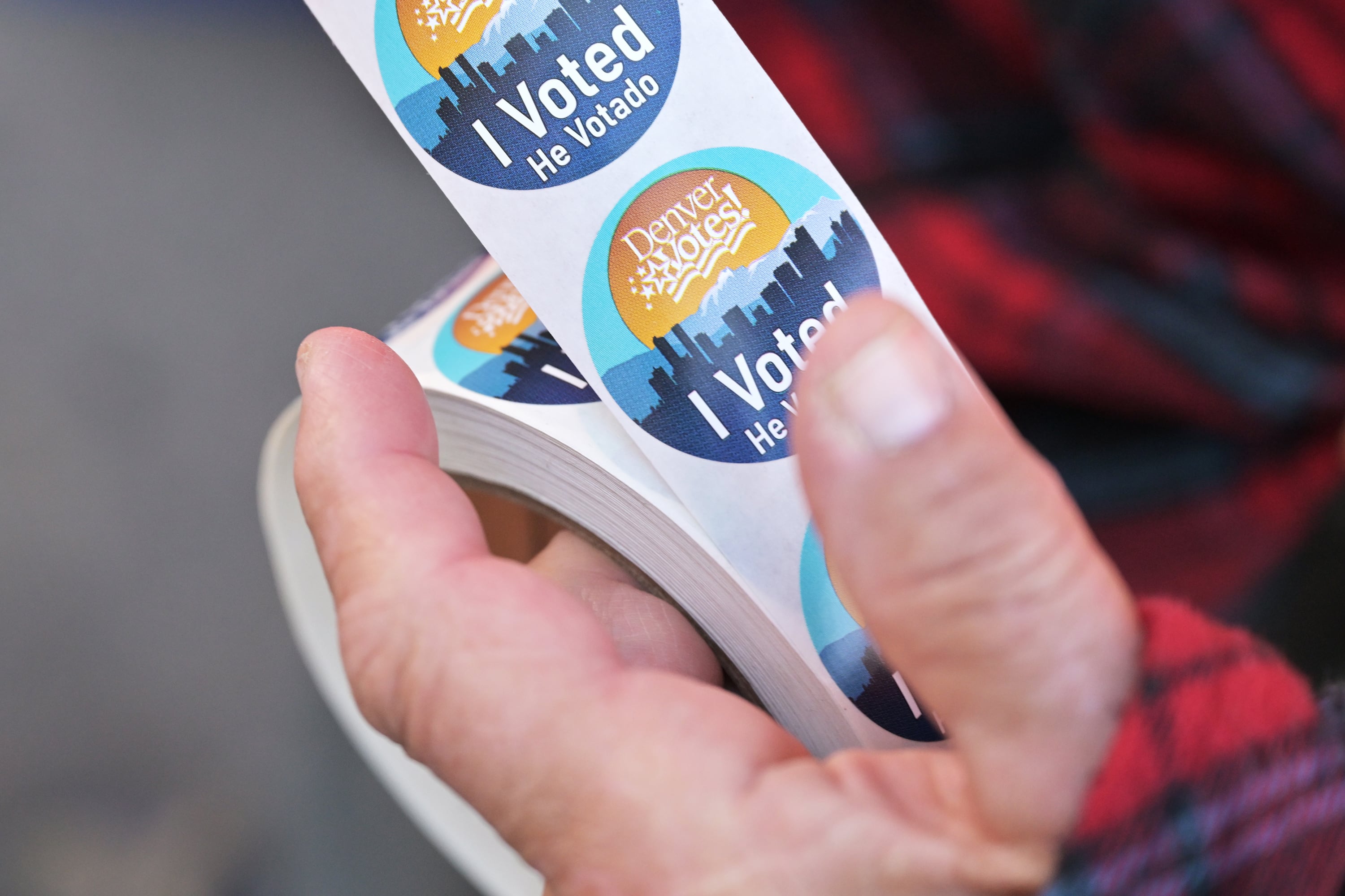 A hand holds a roll of voting stickers with a red flannel sleeve on the side.