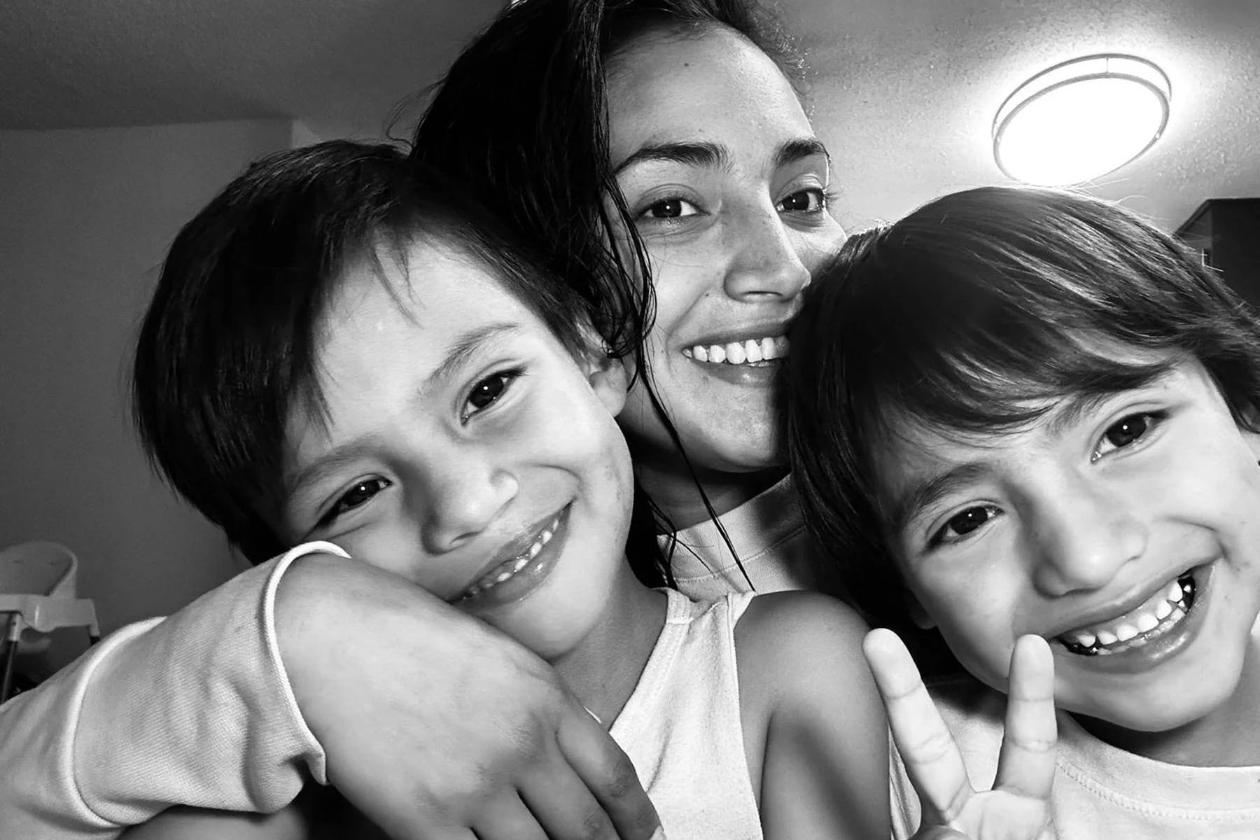 A black and white photograph of a mom and her two sons smiling at the photo while embracing.