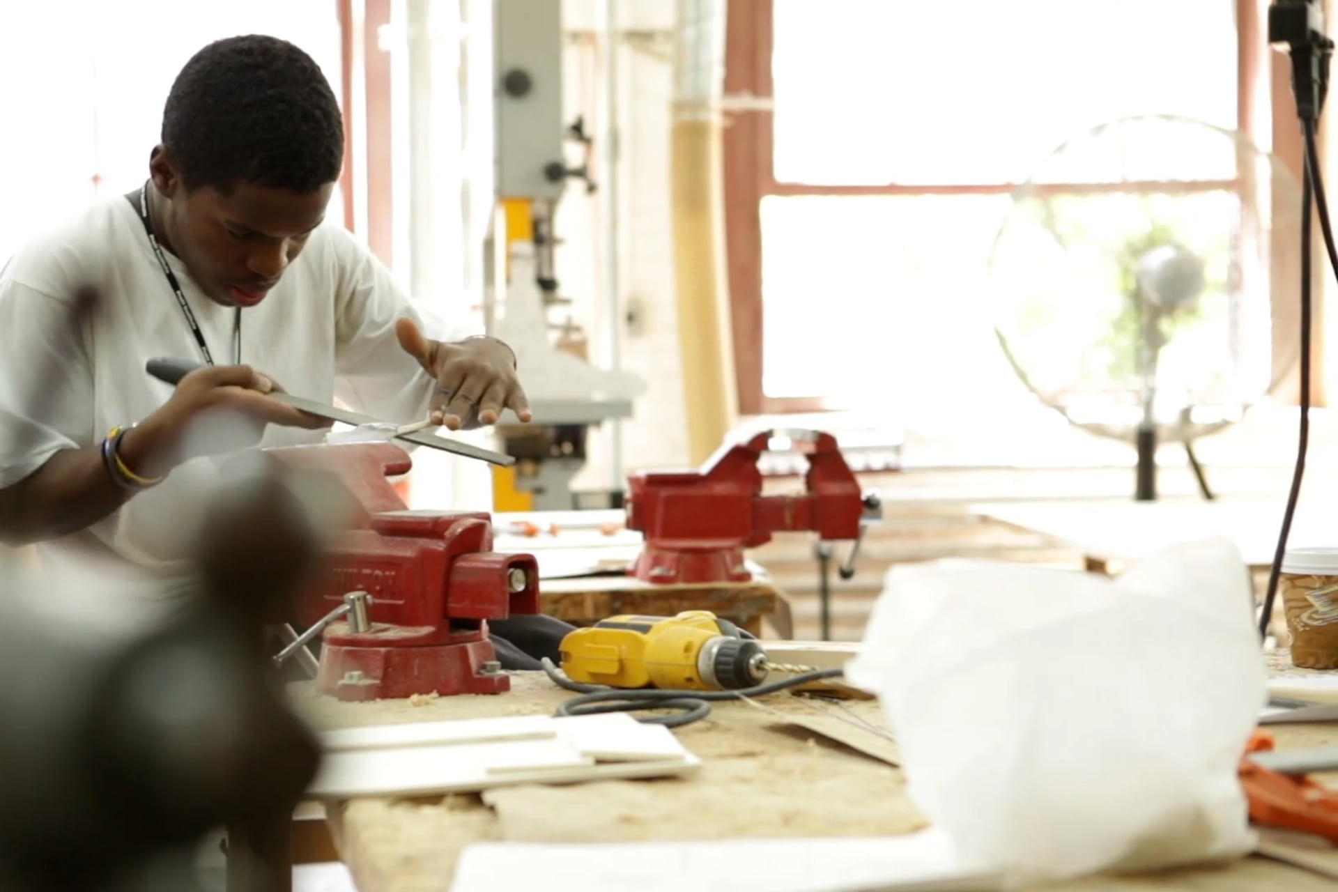 A boy in a white T-shirt uses tools to build something.
