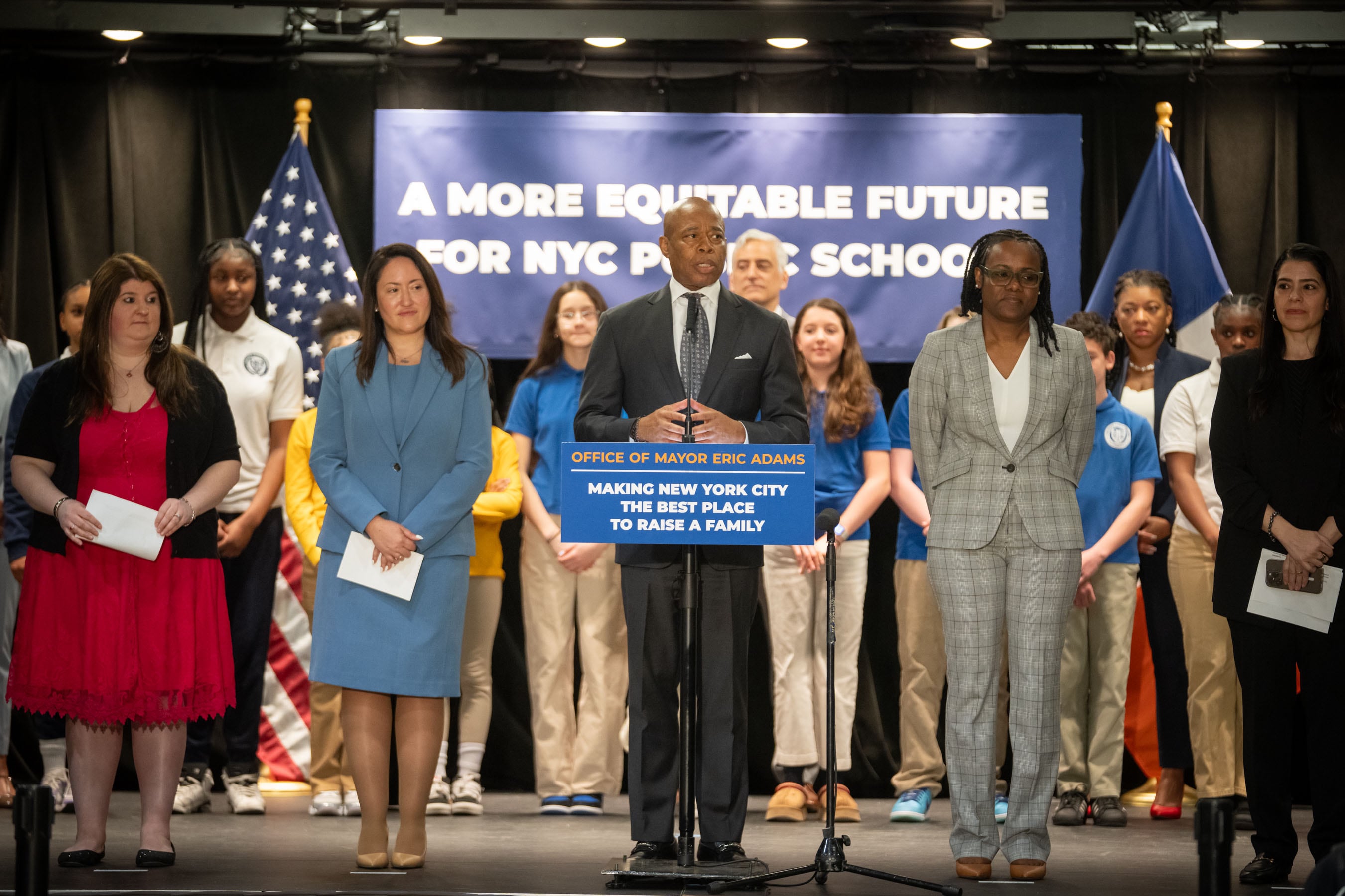A man in a suit stands at podium surrounded by others in business attire.