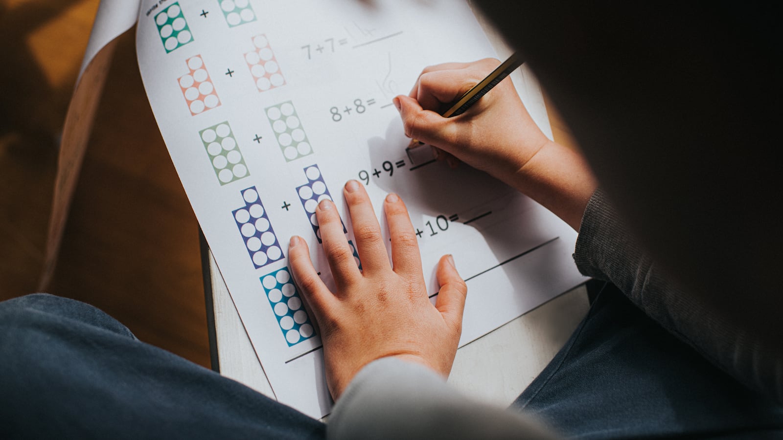 Child adding numbers on a printed maths sheet of homework. Space for copy.