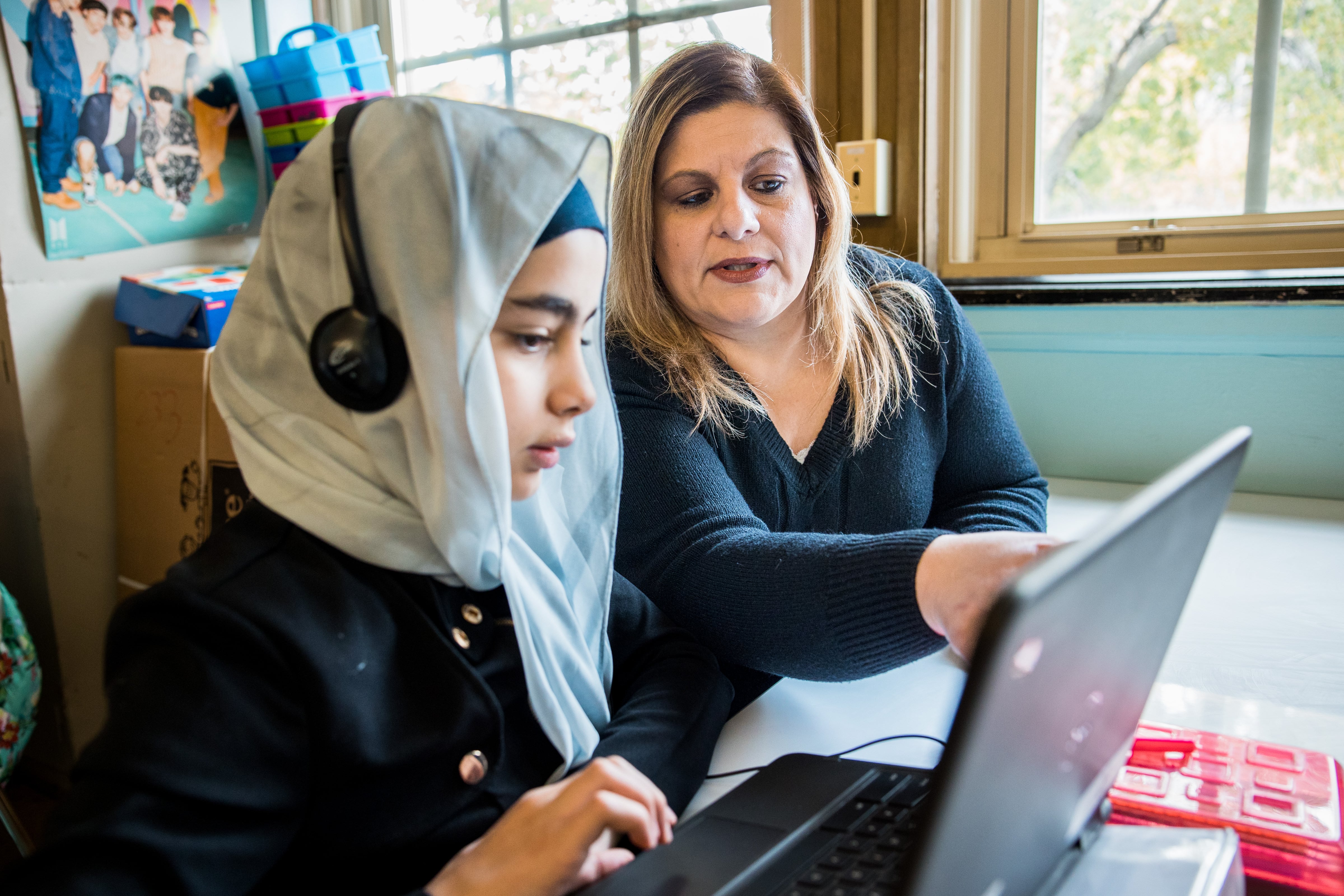 A woman works alongside a girl on a laptop.
