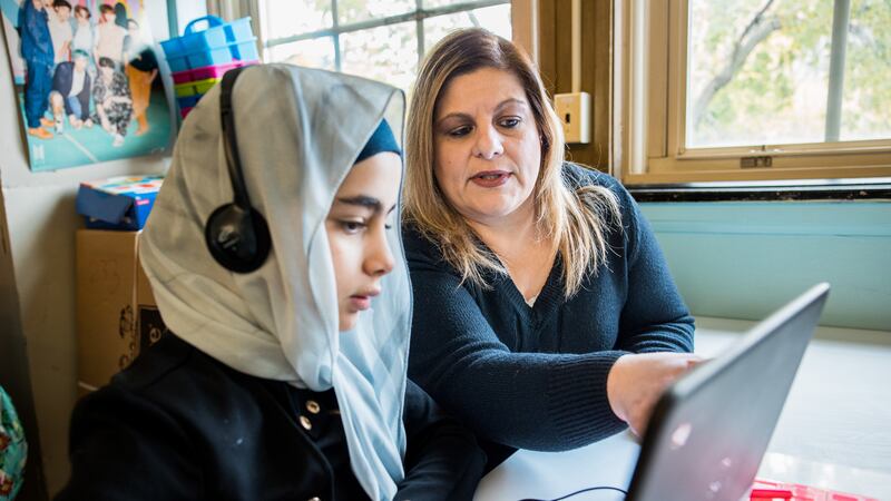 A woman works alongside a girl on a laptop.
