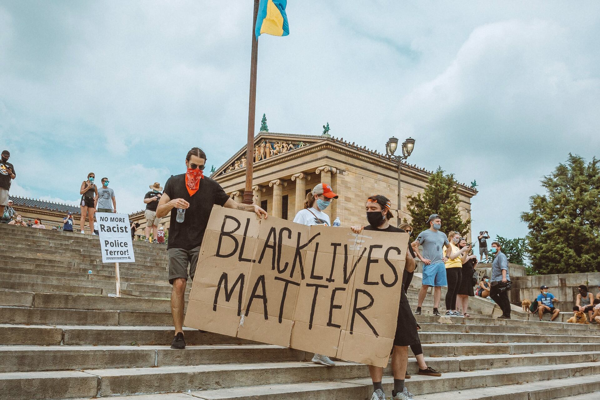 Protestors walking down the Art Museum steps holding a large cardboard sign that reads Black Lives Matter.