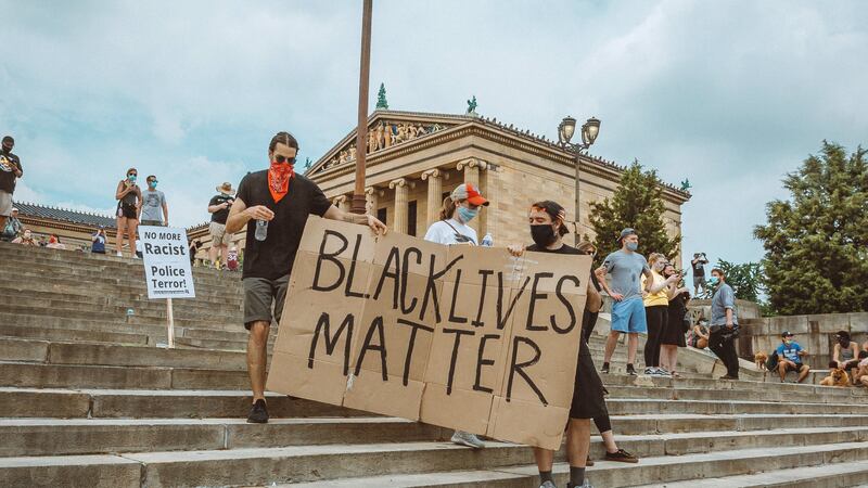 Protestors walking down the Art Museum steps holding a large cardboard sign that reads Black Lives Matter.