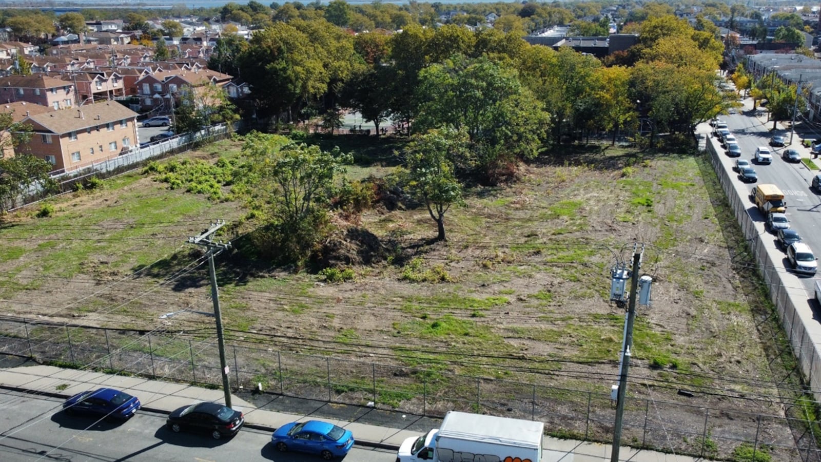 Patches of dirt and grass, as well as a few trees, cover a fenced off lot near P.S. 312 in Brooklyn.