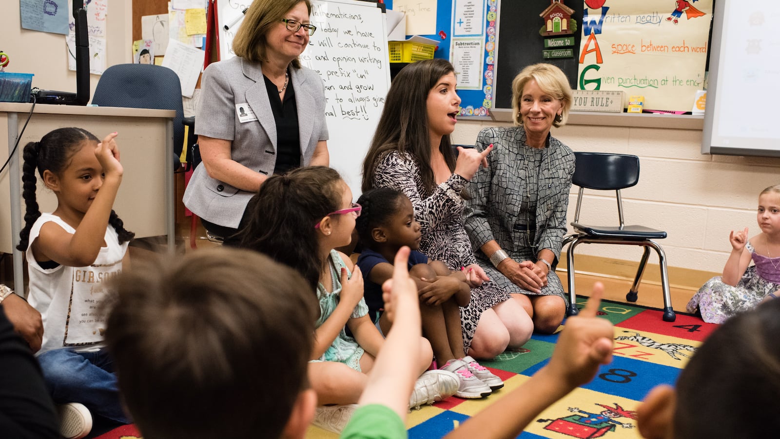 Education Secretary Betsy DeVos, right, sits on the floor during the morning meeting with teacher, Angel Snyder, center, and her first grade class in Hanover, New Hampshire in 2018. (photo by Sarah L. Voisin/The Washington Post via Getty Images)