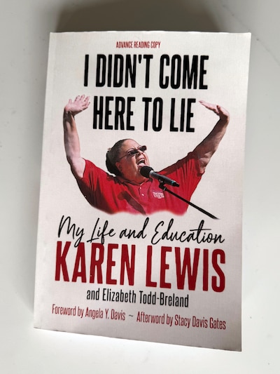 A white book with red and black text and a photograph of a Black woman raising her hands while wearing a red shirt sits on a white table.