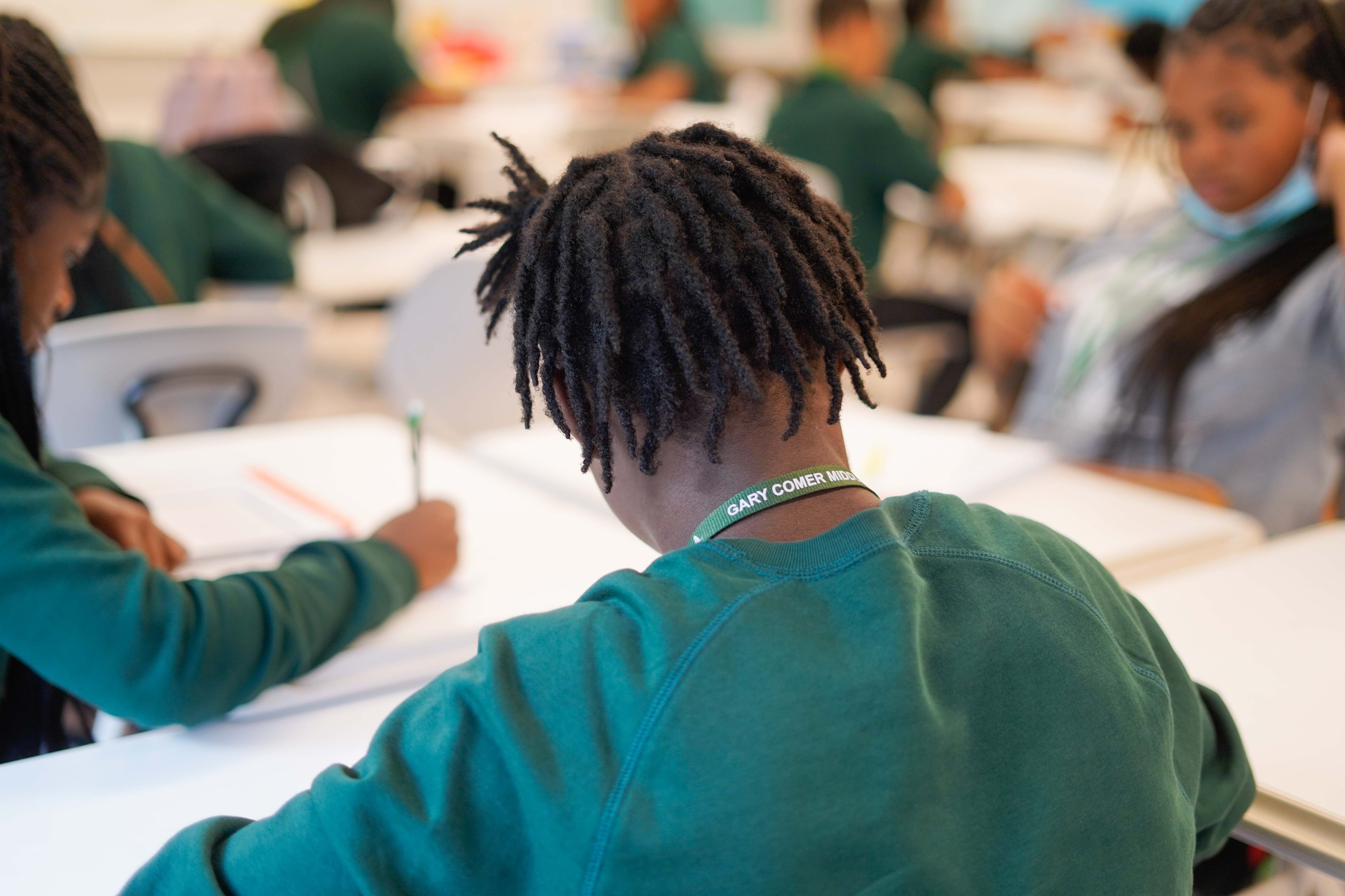 A bird's eye view of middle school students, all wearing green, working at a desk in a classroom.