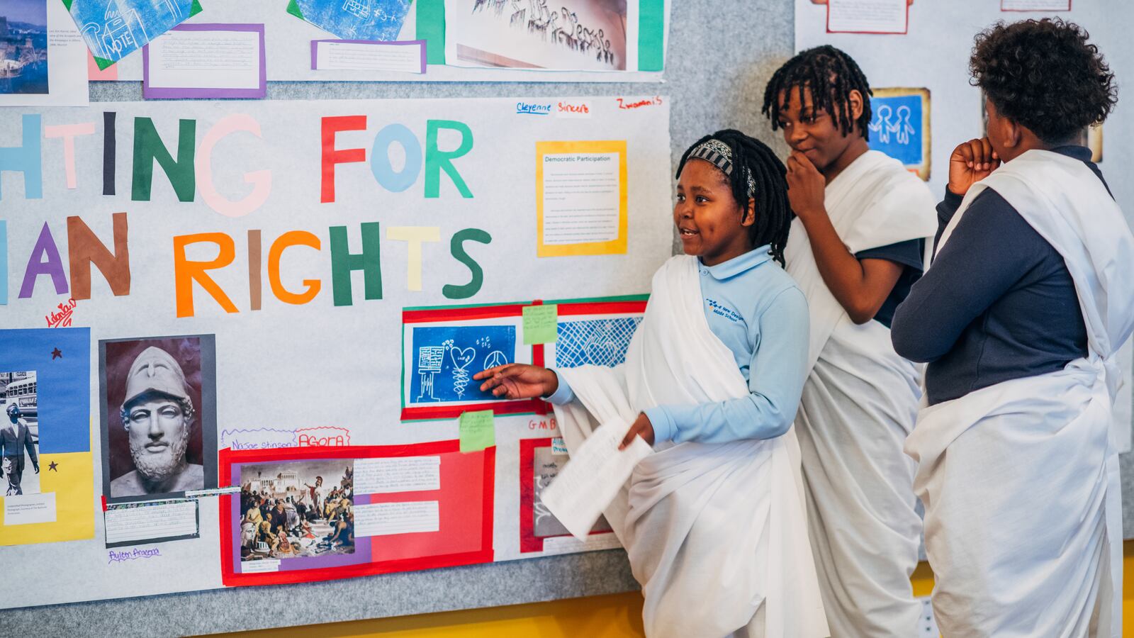 Three students look at a classroom wall display with information about American democracy.
