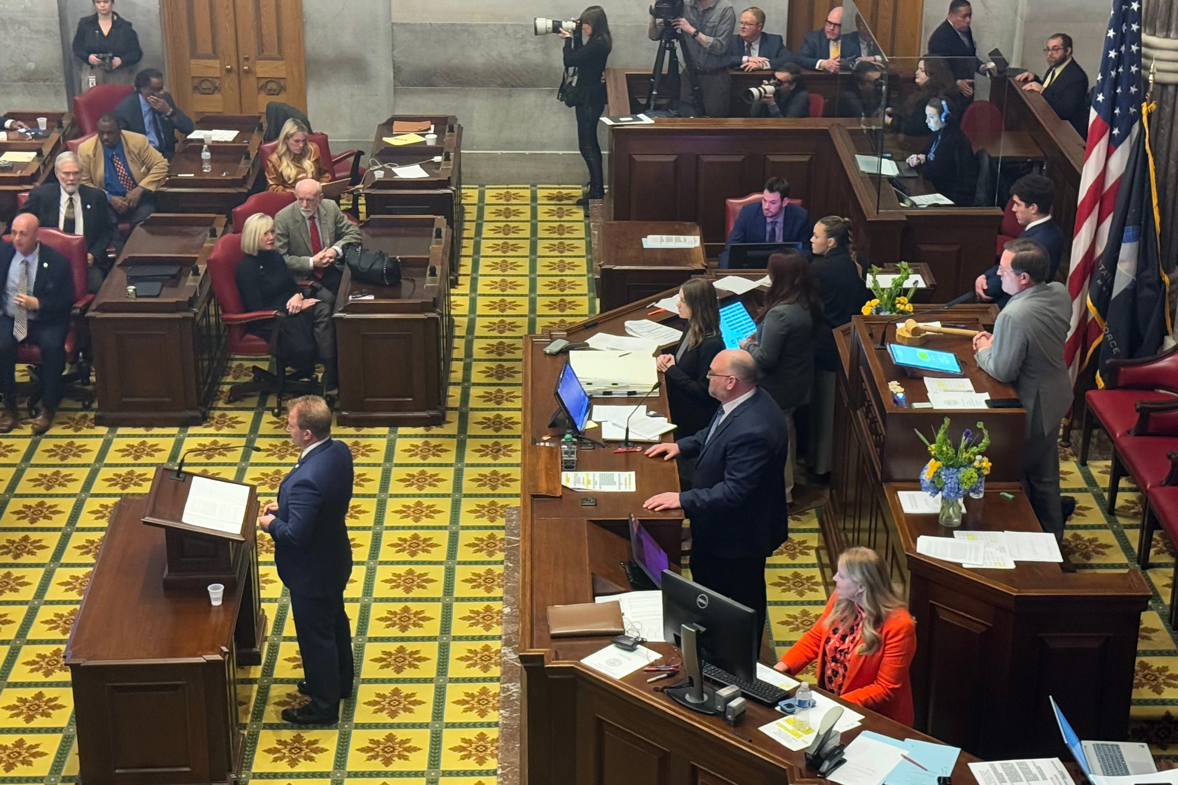 A group of people in suits stand on the floor of a capitol building.