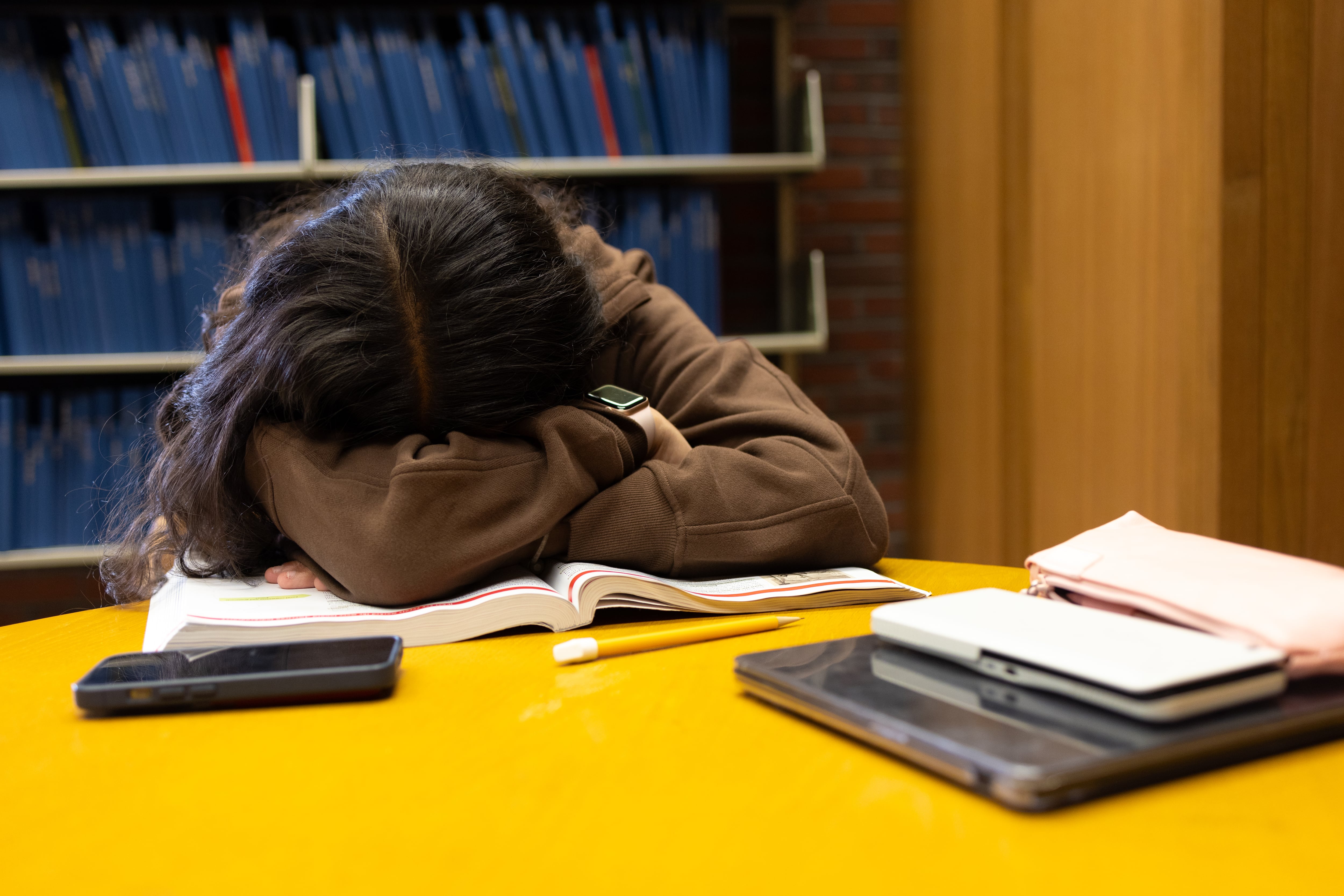 A photograph of a student sleeping at a desk in a library.