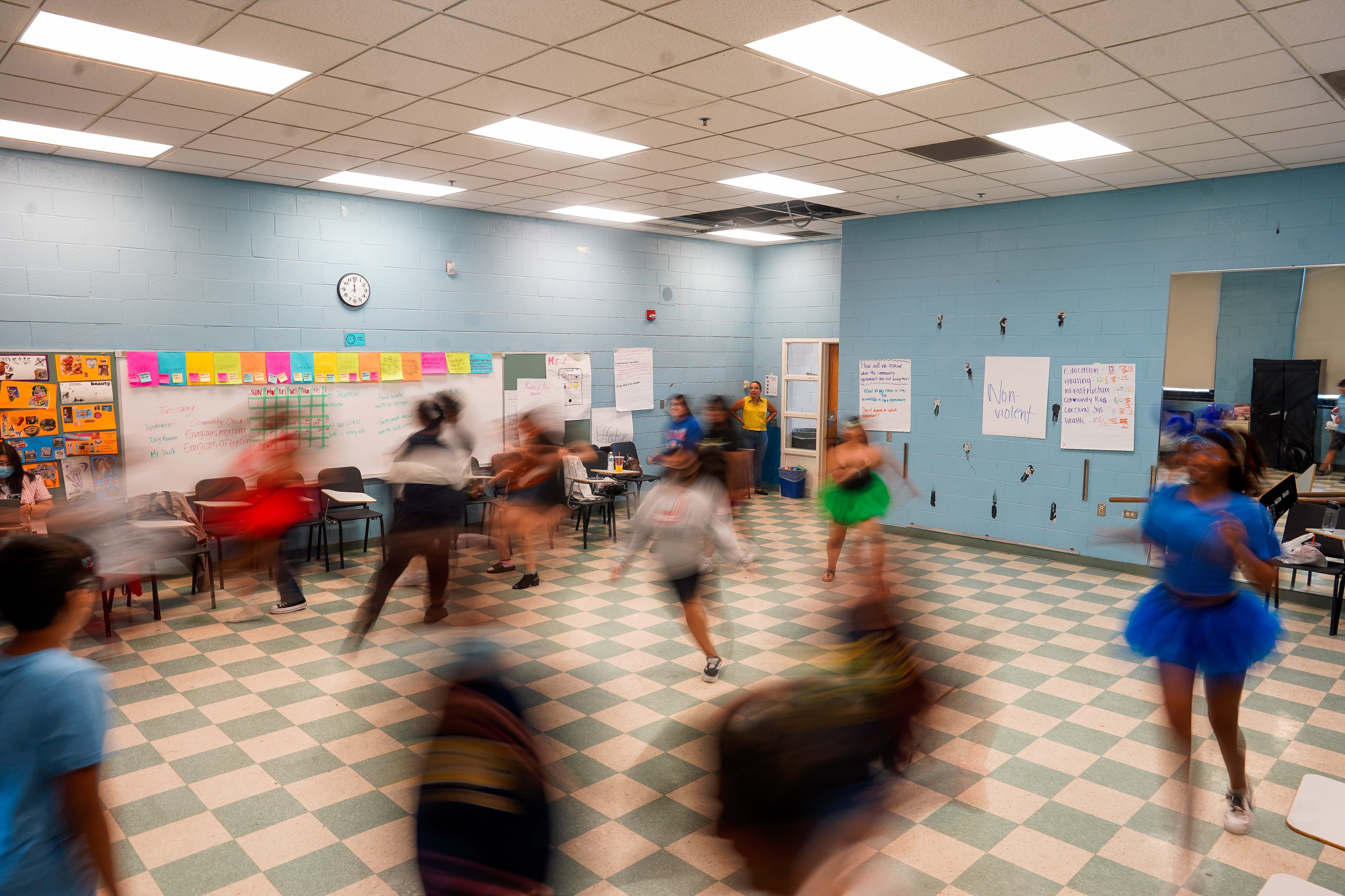 A room with blue walls and a checkered floor with students dancing who are blurred by the motion.