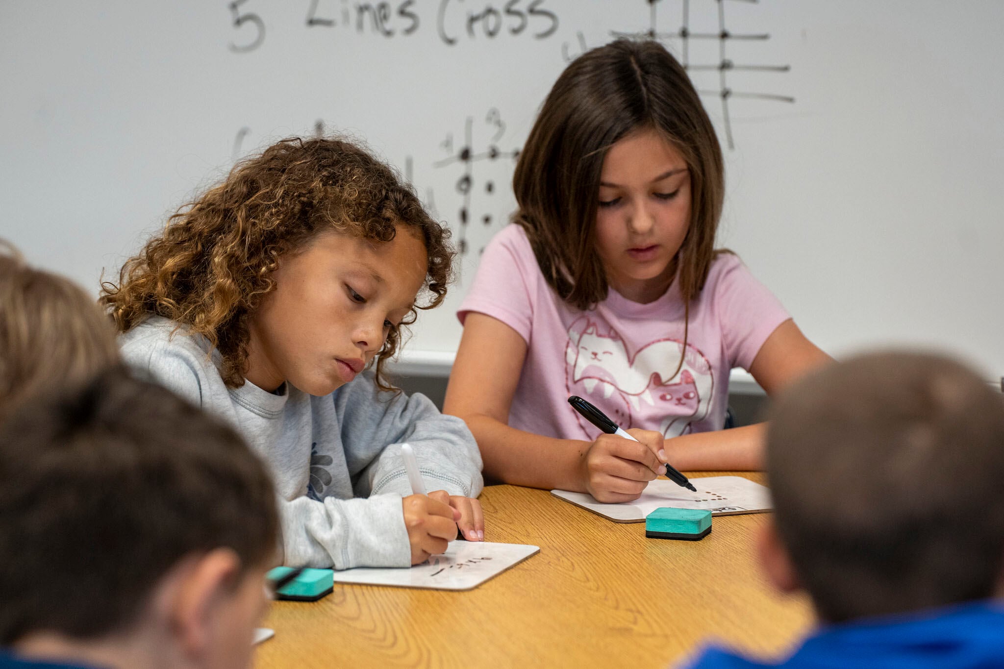 Two young students work at a desk in a classroom.